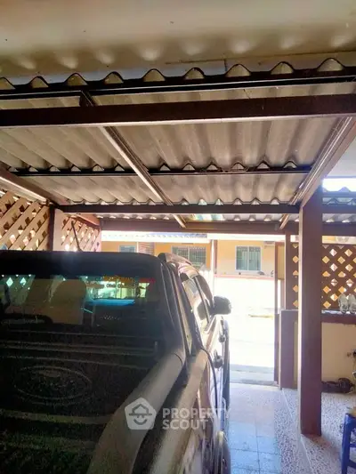 Covered parking area with vehicle under a corrugated metal roof, showcasing residential building exterior.