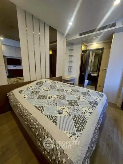 Modern bedroom with stylish decor and cozy quilted bedspread, featuring elegant lighting and wooden flooring.