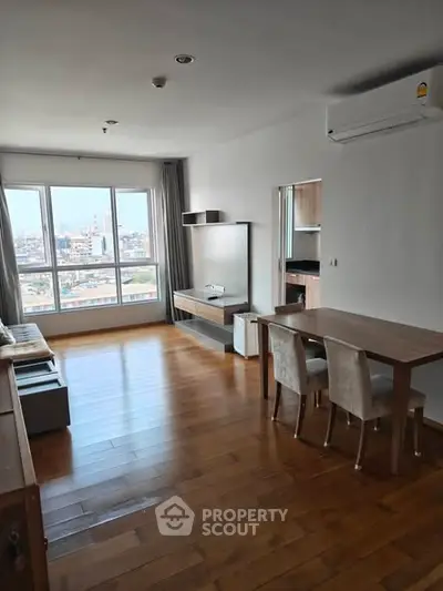 Spacious living room with wooden flooring and city view, featuring modern furniture and air conditioning.