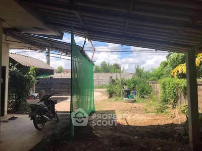 Spacious outdoor area with partial roof and greenery, ideal for versatile use.