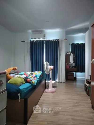 Cozy bedroom with wooden flooring and stylish curtains, featuring a comfortable bed and a dressing table.
