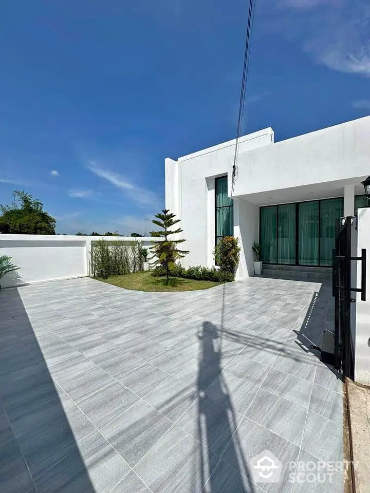 Modern white house with spacious tiled driveway and lush greenery under clear blue sky.