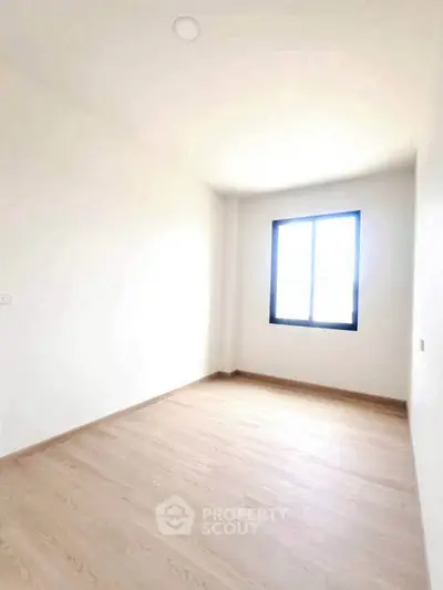 Bright empty room with wooden flooring and large window, perfect for customization.