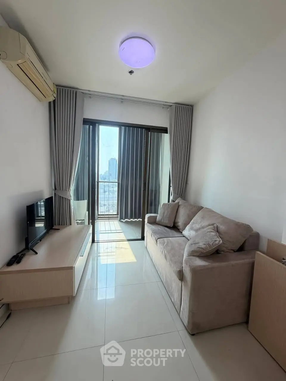 Cozy living room with modern sofa and city view balcony in high-rise apartment.