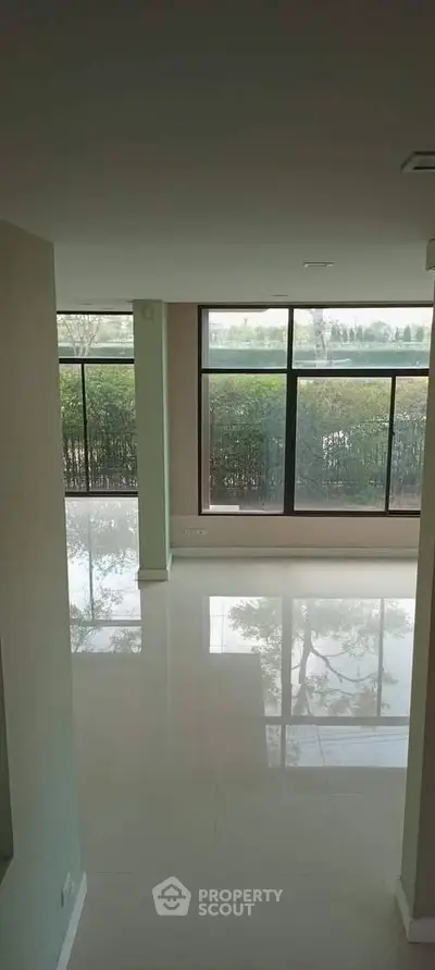 Spacious living room with large windows offering a serene garden view, perfect for natural light lovers.