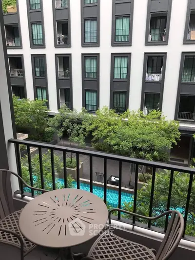 Charming balcony view overlooking lush greenery and modern apartment building with pool.