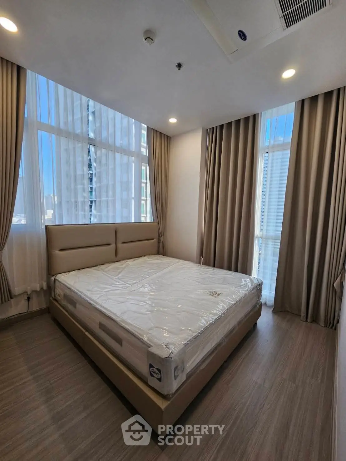 Spacious bedroom with large windows and modern furnishings in a high-rise apartment.