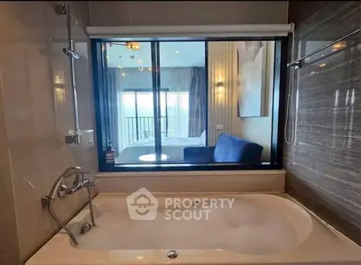 Luxurious bathroom with bathtub and window view into a stylish bedroom.