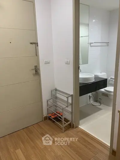 Modern apartment entrance with adjacent bathroom featuring sleek fixtures and wooden flooring.