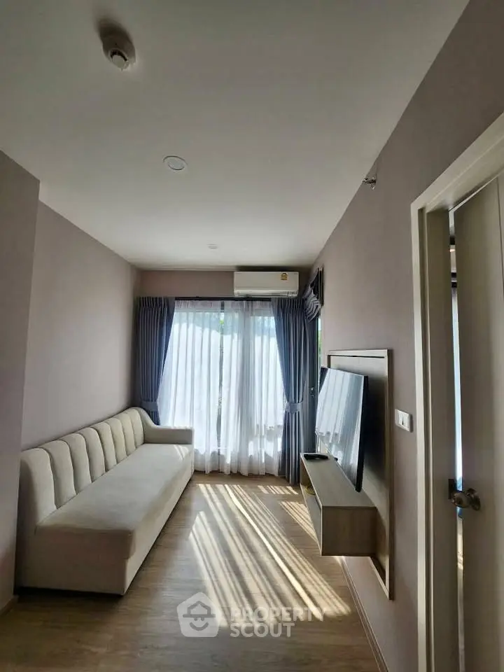 Modern living room with natural light, featuring a sleek sofa and wall-mounted TV, perfect for relaxation.
