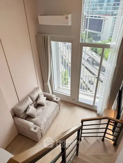 Modern loft apartment with large windows and cozy seating area, offering stunning city views.