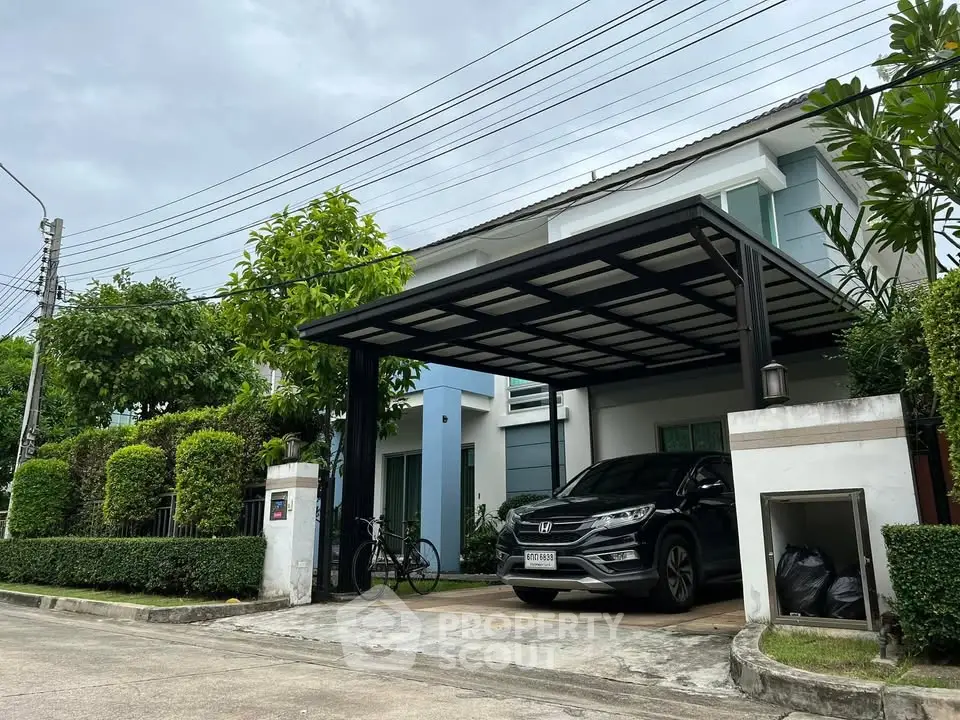 Modern two-story house with carport and lush greenery in a serene neighborhood.