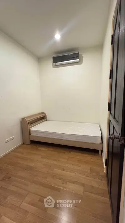 Cozy bedroom with wooden flooring and air conditioning, perfect for a minimalist lifestyle.