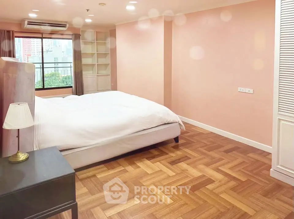Spacious bedroom with parquet flooring and large window offering city views.