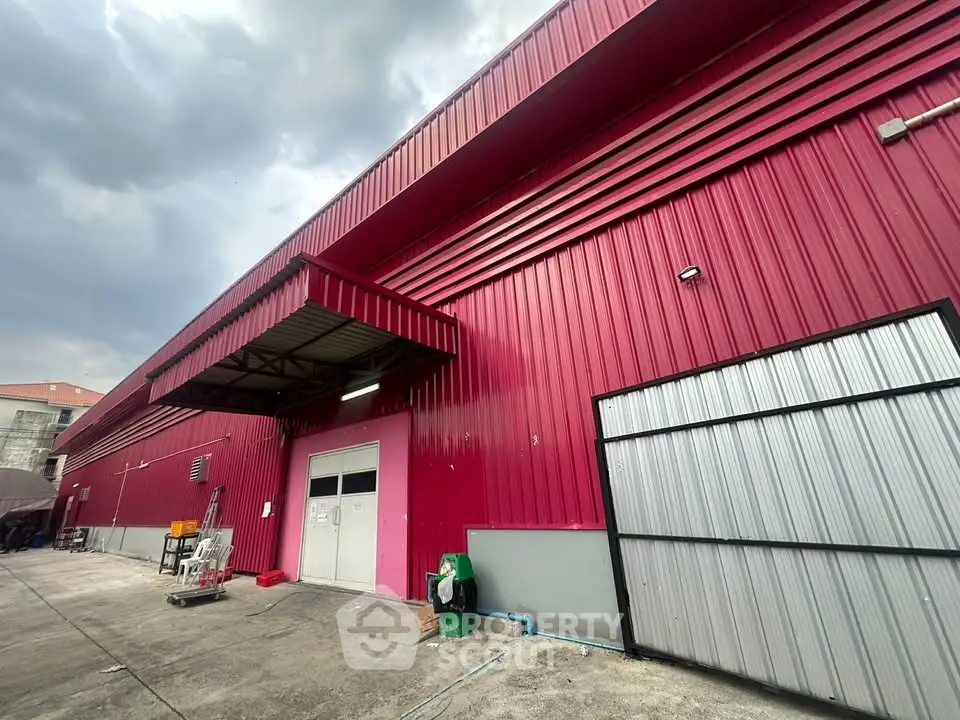 Vibrant red industrial warehouse exterior with large doors and spacious concrete yard.