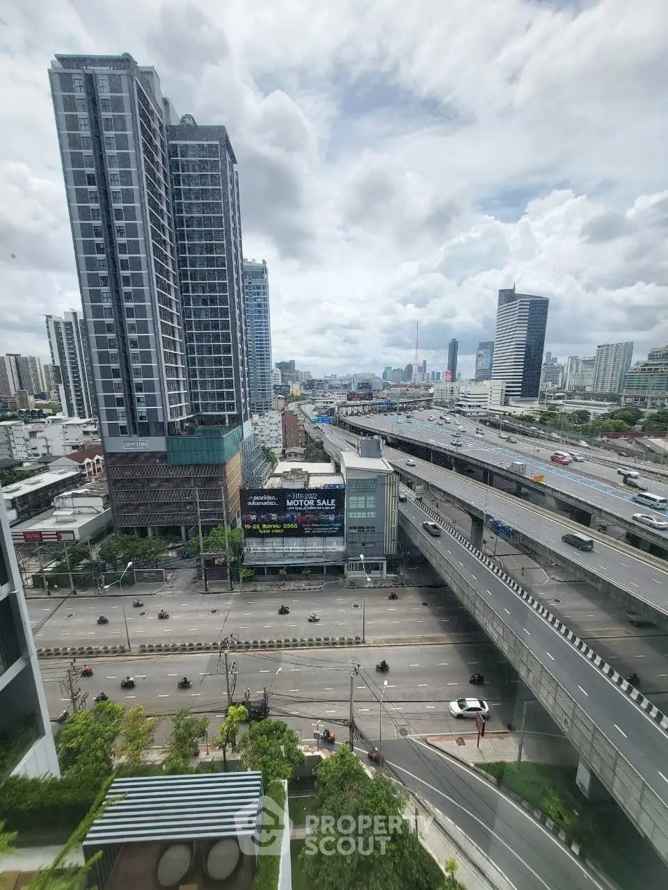 Stunning cityscape view from high-rise building with highway and skyscrapers under a cloudy sky.