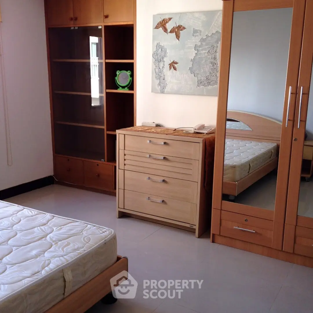 Spacious bedroom with wooden furniture and mirrored wardrobe in modern apartment.