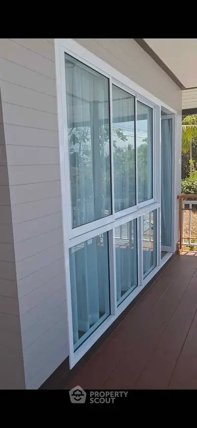 Modern balcony with large sliding glass windows and wooden flooring, offering a serene outdoor view.