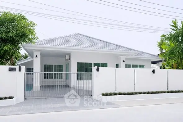 Modern single-story white house with gated entrance and lush greenery.