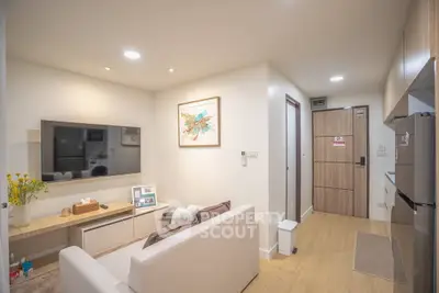 Modern living room with sleek decor and open kitchen layout, featuring a cozy sofa and wall-mounted TV.