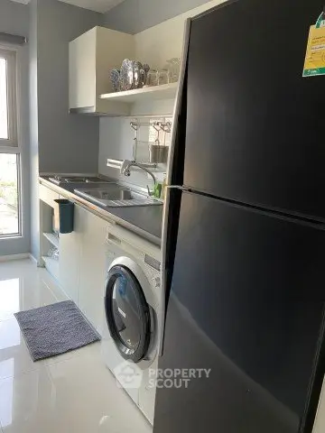 Modern kitchen with sleek appliances and ample natural light, featuring a washing machine and large fridge.