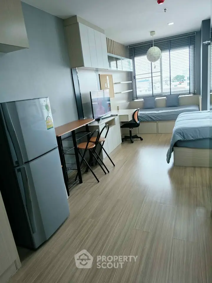 Modern studio apartment with sleek design, featuring a cozy bed, workspace, and kitchen area with a fridge.