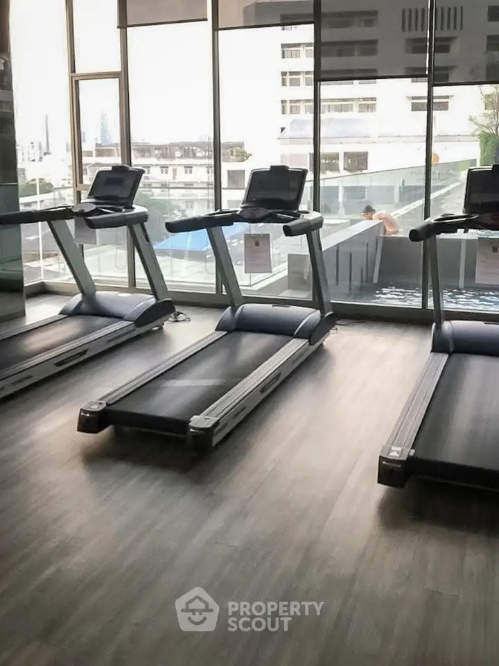Modern gym with treadmills and pool view in luxury apartment building.