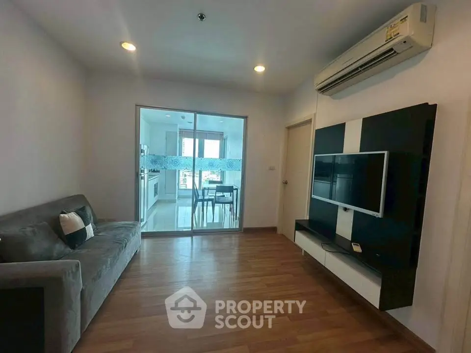 Modern living room with air conditioning and TV, open view to kitchen area.