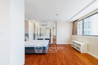 Spacious bedroom with hardwood floors and large window in modern apartment.