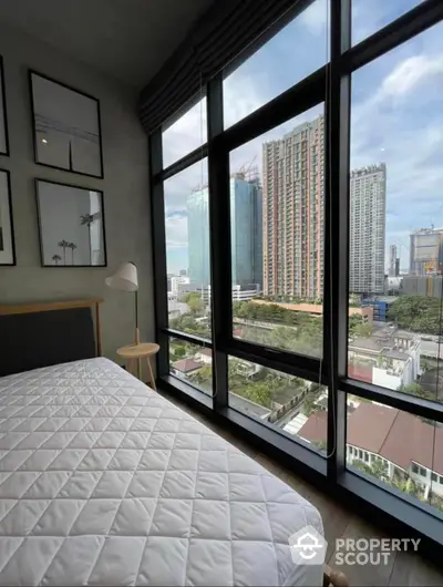 Modern bedroom with floor-to-ceiling windows offering a panoramic cityscape view, complemented by tasteful decor and natural light.