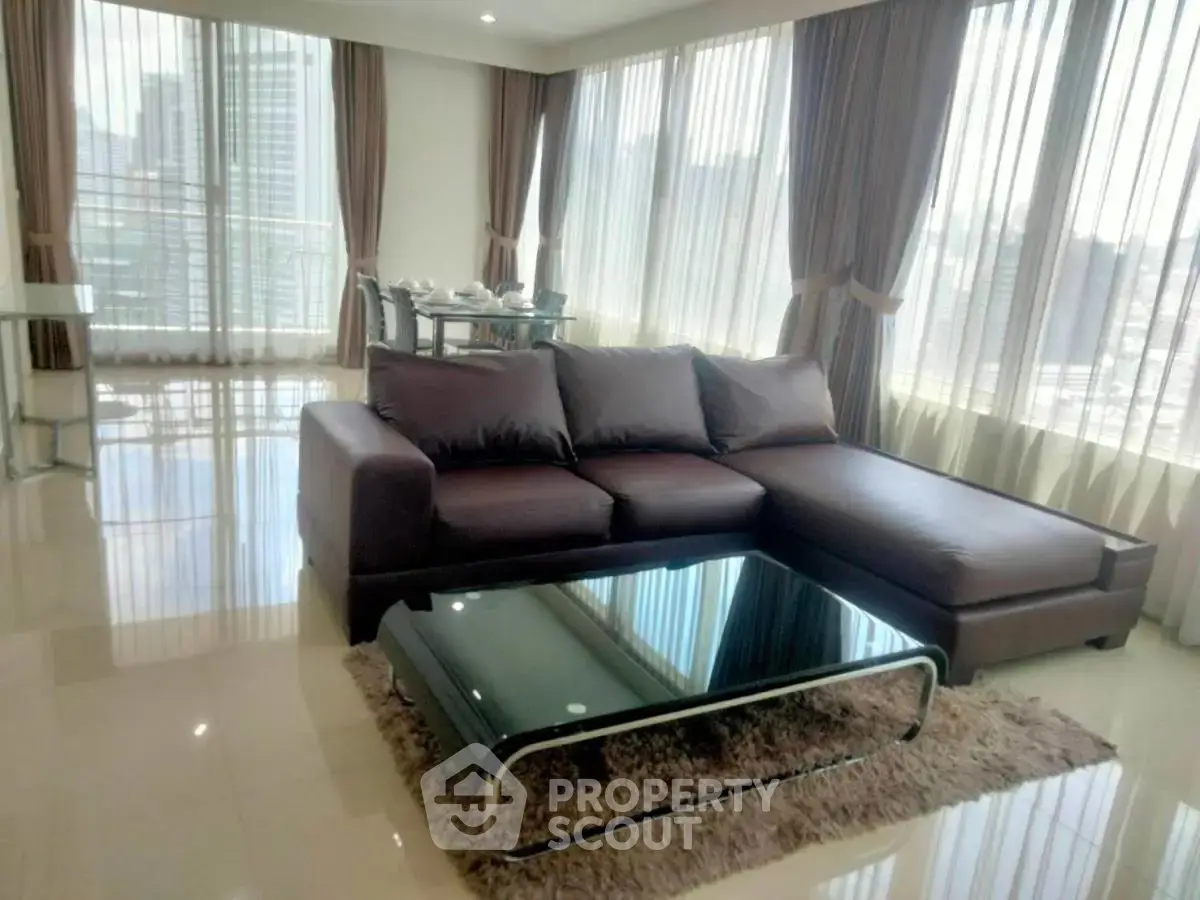 Spacious modern living room with city view, featuring elegant furniture and floor-to-ceiling windows.