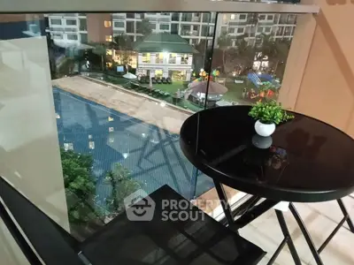 Chic balcony with glass railing overlooking a luxurious pool and vibrant community area.