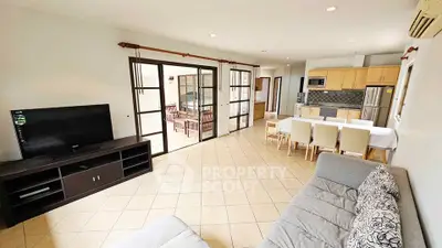 Spacious open-plan living room with modern kitchen and dining area, featuring large windows and tiled flooring.