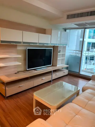 Modern living room with sleek furniture and large TV, featuring floor-to-ceiling windows for natural light.