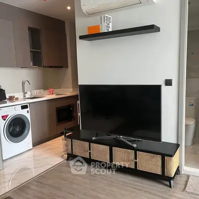 Modern apartment interior with sleek kitchen and cozy living area featuring a TV and washing machine.