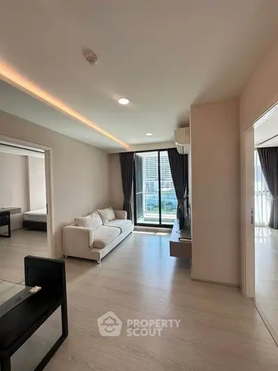 Modern living room with large windows and city view, featuring sleek furniture and natural light.