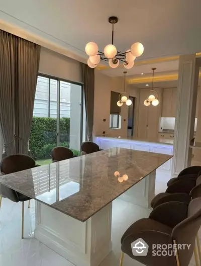 Elegant dining area seamlessly connects to a modern kitchen, featuring a large marble table, chic lighting, and a view of the lush garden.