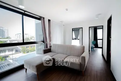 Modern living room with large windows and city view, featuring a stylish sofa and wooden flooring.