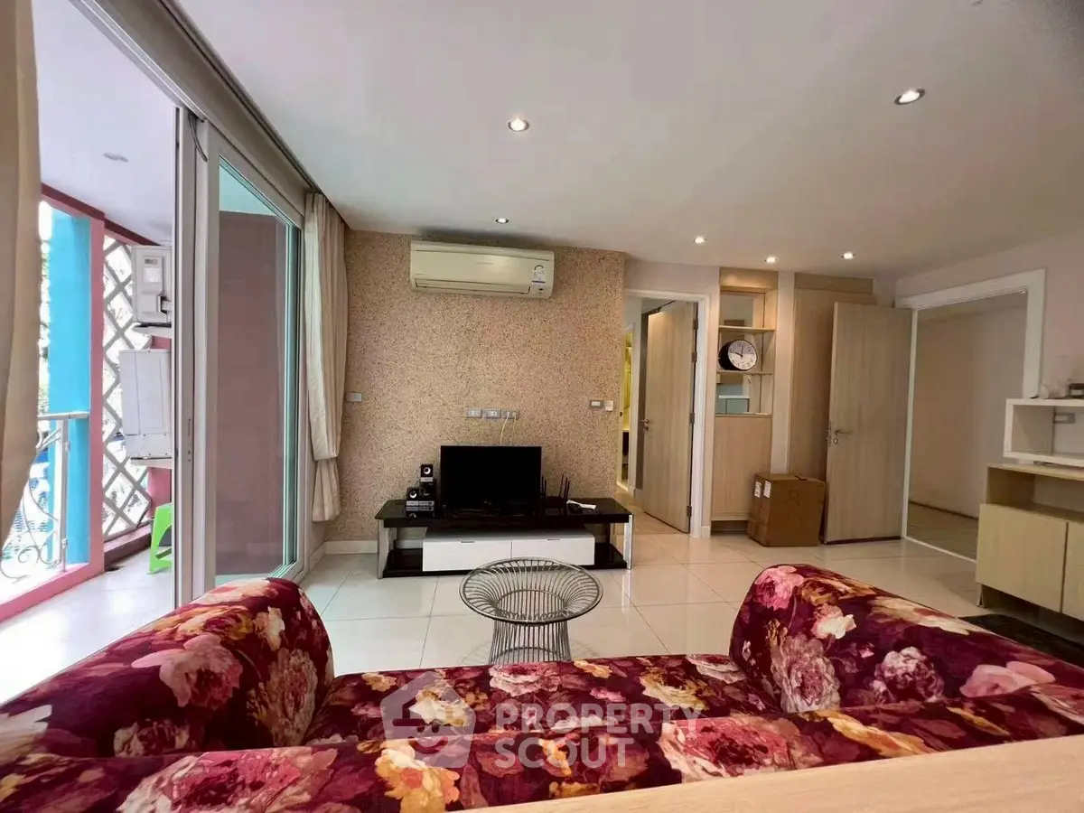 Spacious living room with floral sofa and modern decor, featuring air conditioning and entertainment center.