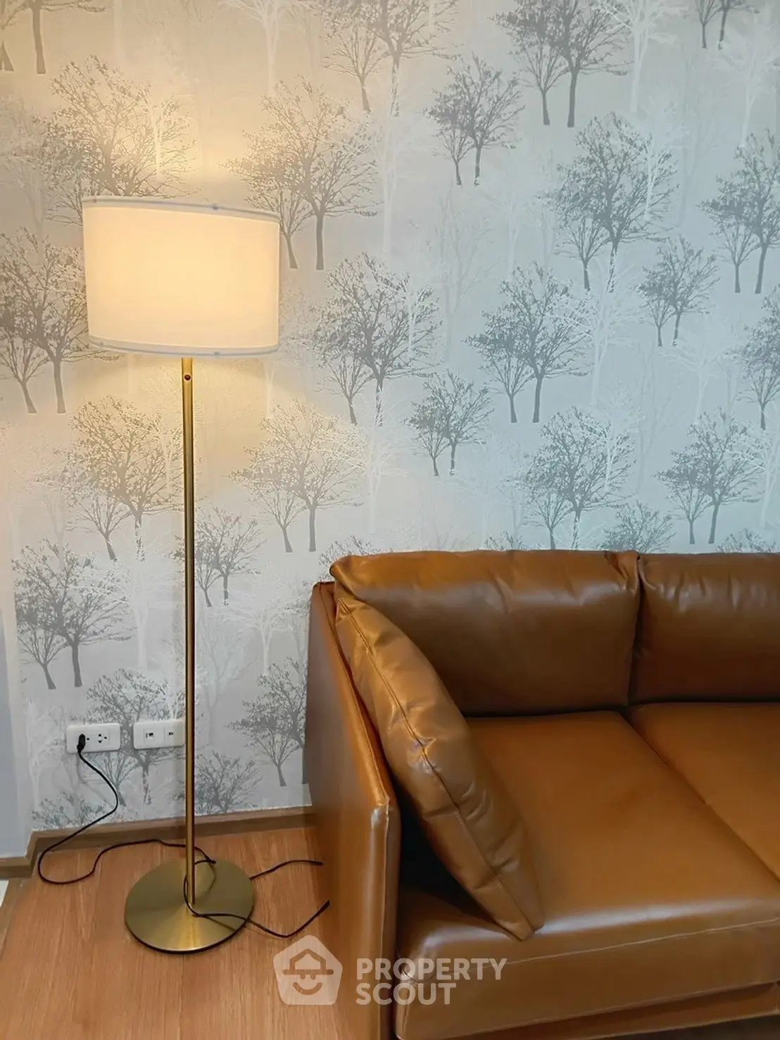 Stylish living room with leather sofa and elegant floor lamp against tree-patterned wallpaper.