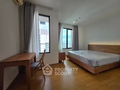 Spacious bedroom with wooden flooring and city view, featuring a bed and study desk.
