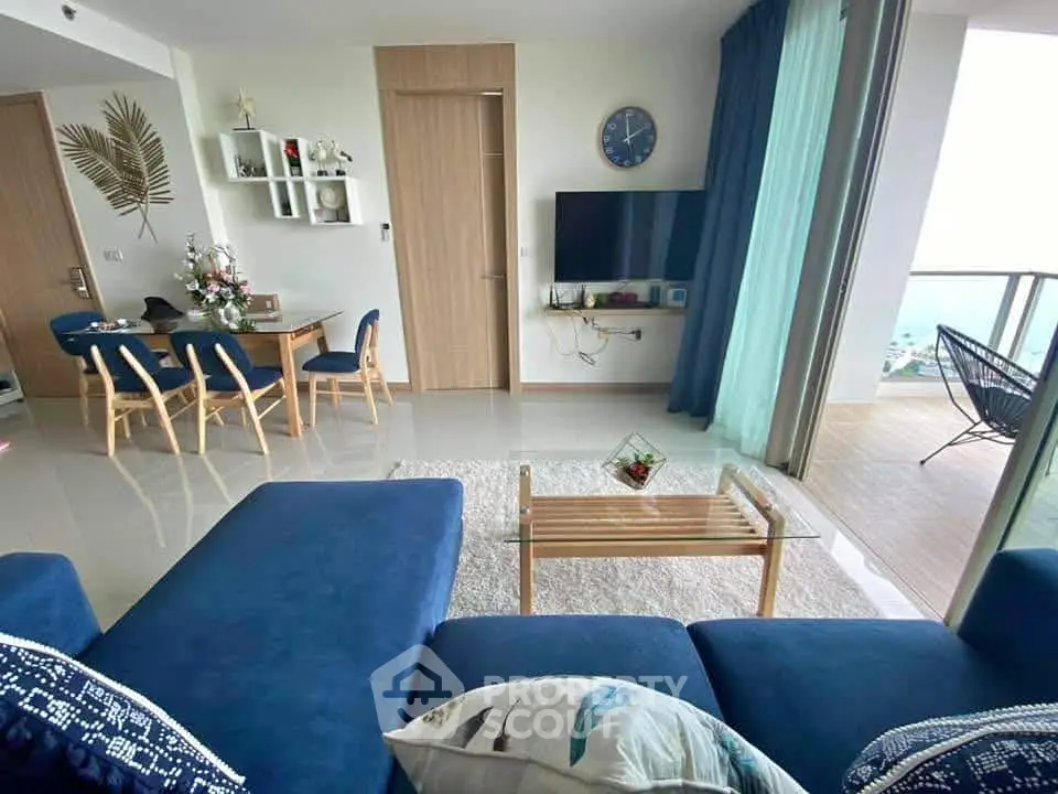 Modern living room with blue sofa, wall-mounted TV, and balcony with ocean view.