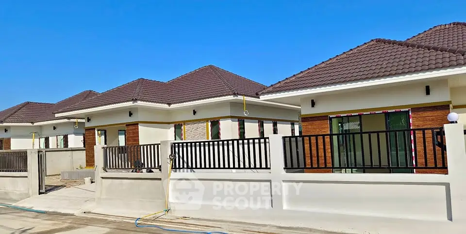 Modern single-story homes with tiled roofs and fenced yards under clear blue sky.