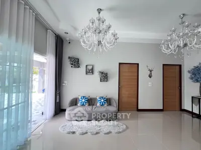 Elegant living room with chandeliers, plush sofa, and large windows for natural light.