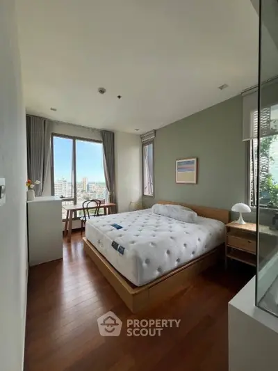 Bright and airy bedroom with large window offering stunning city views, featuring modern decor and wooden flooring.
