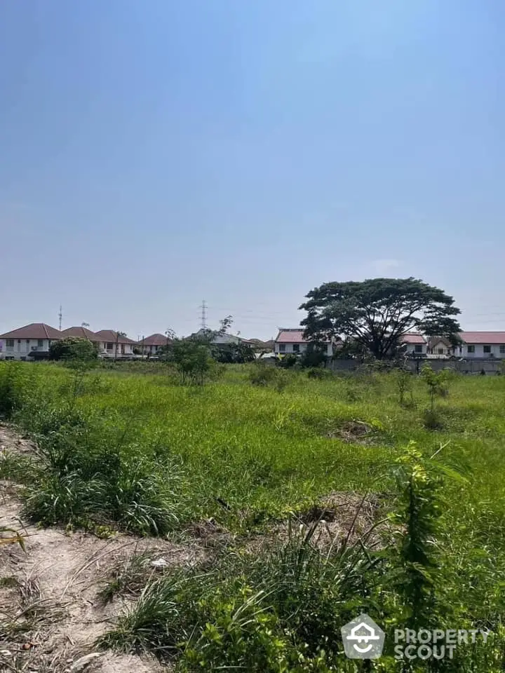 Expansive greenfield land ready for development, surrounded by serene residential area with clear skies and potential for growth.