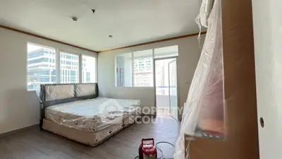 Spacious bedroom with large windows and city view, featuring a covered mattress and balcony access.