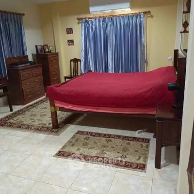 Spacious bedroom with elegant wooden furniture and red bedding, featuring tiled floors and blue curtains.