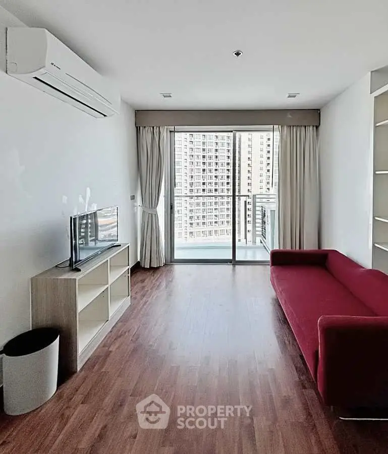 Modern living room with red sofa, TV, and balcony view in high-rise apartment.