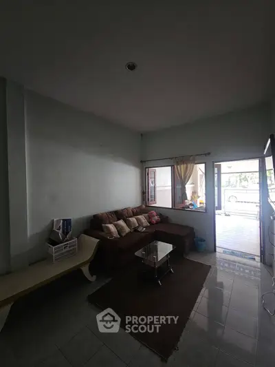 Cozy living room with sectional sofa and glass coffee table, featuring natural light from large windows.